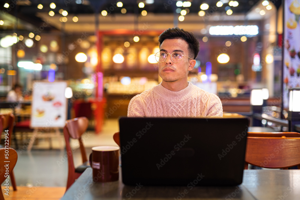 Young man using laptop computer at coffee shop while thinking Young man using laptop computer at coffee shop while thinking