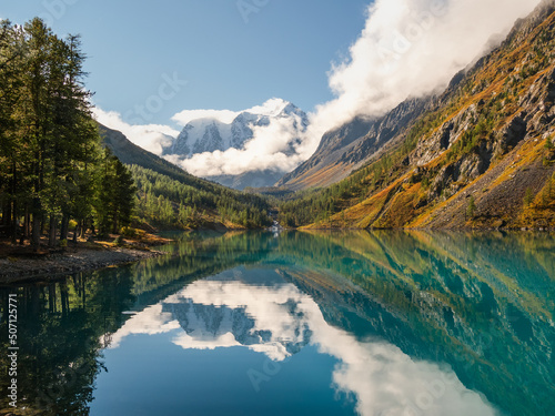 Picturesque mountain lake in the summer day  Bright sunny landscape with glacier reflection in water surface of mountain lake under clear sky. Beautiful reflection of mountains  sky and white clouds
