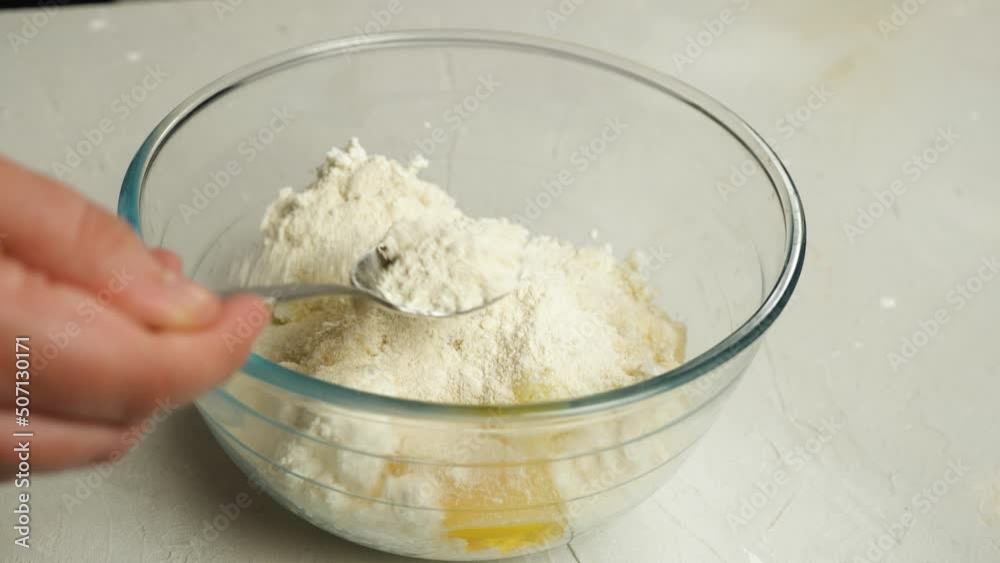 The cook sprinkles flour on a broken chicken egg with sugar and homemade cottage cheese in a glass cup. Close-up. Cooking lazy dumplings with cottage cheese The cook sprinkles flour on a broken chicken egg with sugar and homemade cottage cheese in a glass cup. Close-up. Cooking lazy dumplings with cottage cheese