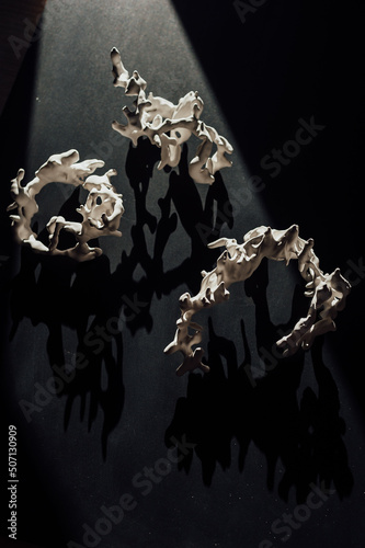 abstract white figurine in the shape of a coral on a black background in the rays of sunlight