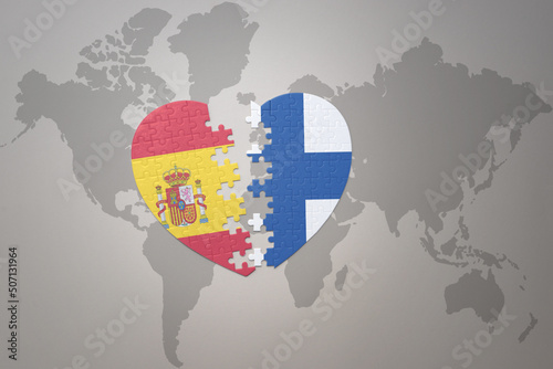 puzzle heart with the national flag of finland and spain on a world map background. Concept.
