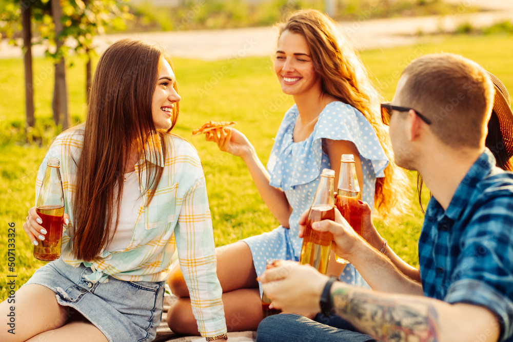 group of friends are enjoying pizza in the park. Men and women sit on the grass around a pizza box group of friends are enjoying pizza in the park. Men and women sit on the grass around a pizza box