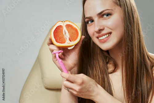 a young beautiful woman holds a half of a grapefruit and a razor in her hands, a symbol of hair removal on a deep bikini area. female genital hair removal photo
