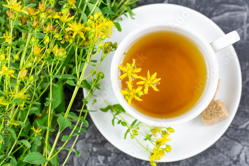 A drink (infusion, decoction) from St. John's wort in a white cup on a saucer on a black (dark) background. Herb and flowers of the medicinal plant Hypericum, Hypericaceae.