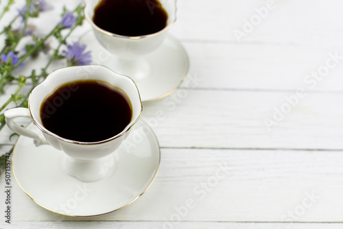 Two cups on saucers with a chicory drink on a white wooden background. Place for the text, ingredient, recipe. A useful substitute for coffee.