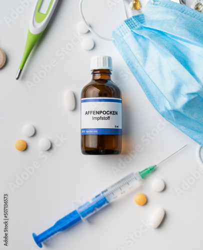 Monkeypox new virus vaccine in german language - Affenpocken Impfstoff bottle on white background with injection face mask and pills