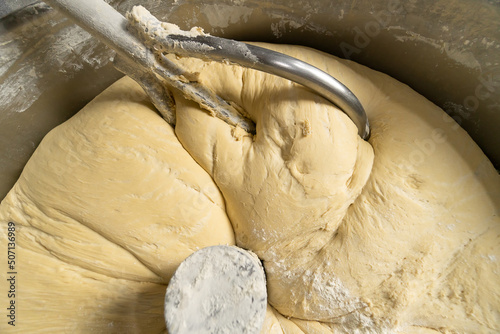 Fotografie Close-up of kneading elastic dough for bread in a kneading machine in a bakery