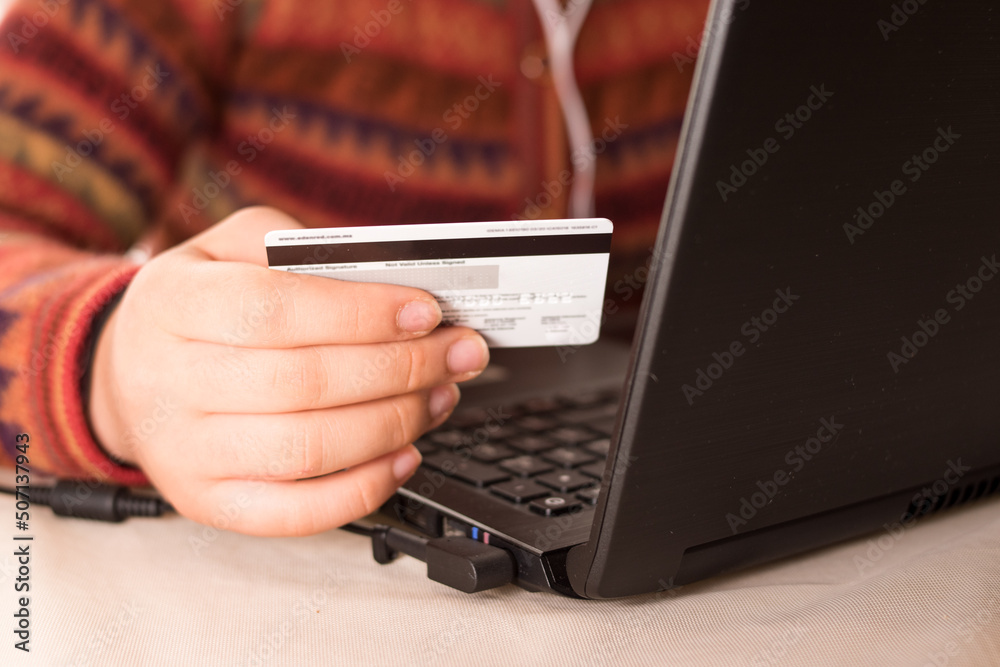 Woman wearing a sweater, holding a credit card and lokking her black laptop Woman wearing a sweater, holding a credit card and lokking her black laptop