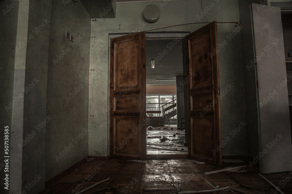 Dark abandoned room. Opened door. Shabby walls. Light in the windows in the background. Wooden old door in an abandoned building.