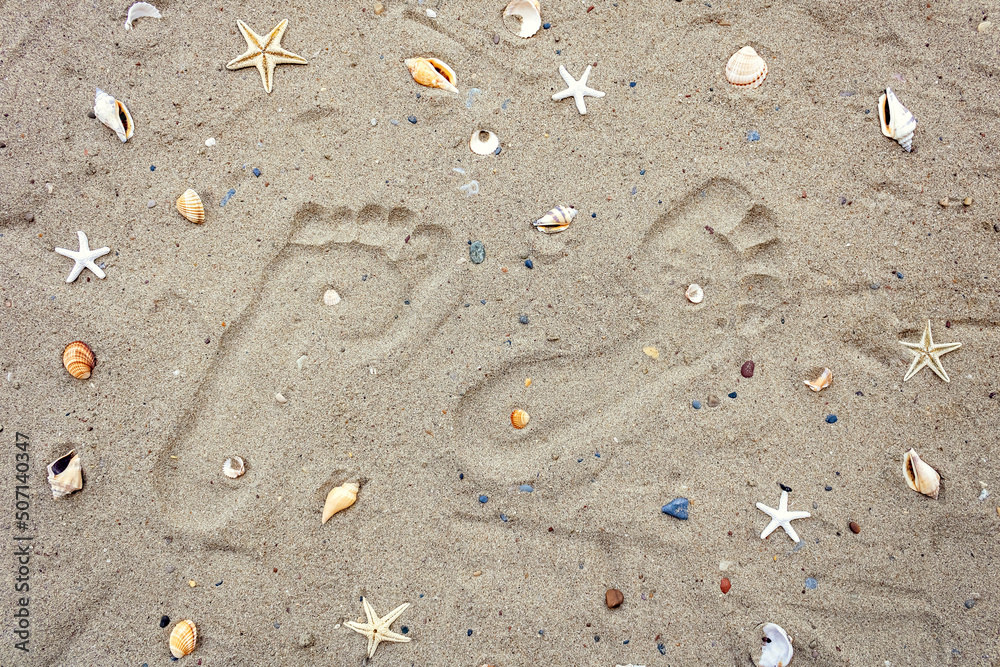 Close-up of two footprints on dry beach sand among seashells and starfish