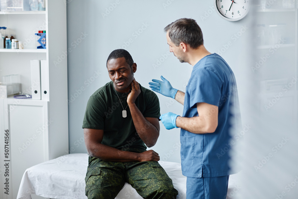 Obraz premium Young Black soldier sitting on medical couch in modern military hospital telling doctor about pain in neck