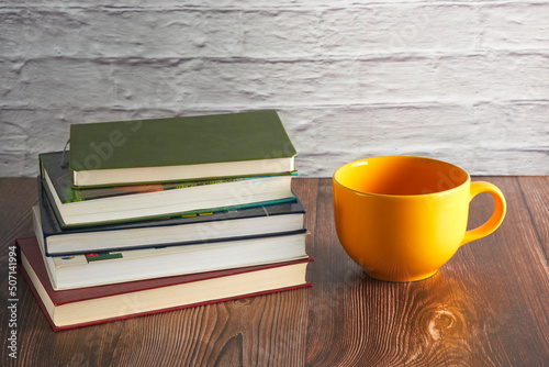 large yellow mug and a stack of books on a table against a brick wall background