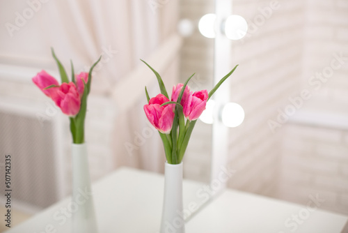 Beautiful pink tulips in vase on table in beauty salon  spring decor 