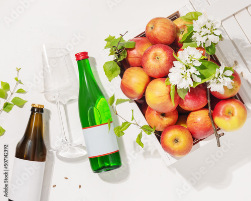 Bottles of natural apple cider with wine glass and farm apples in a white wooden box on a white background. Summer Refreshing Low-alcohol fruit drink. Apples product. Soft focus style, flat lay