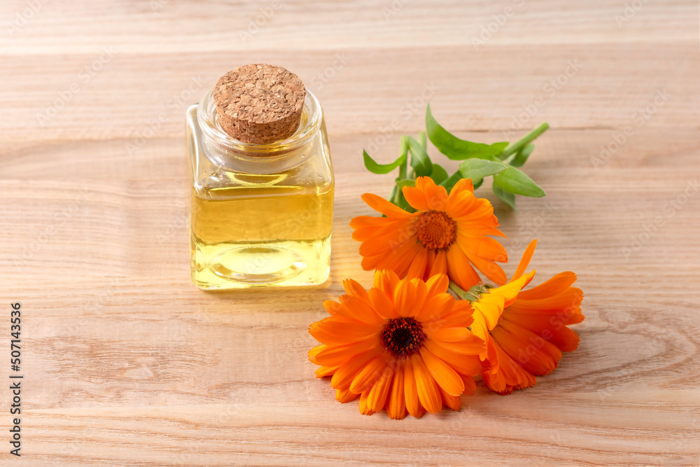 Bottle of essential oil and calendula flowers on a wooden table. - obrazy, fototapety, plakaty 