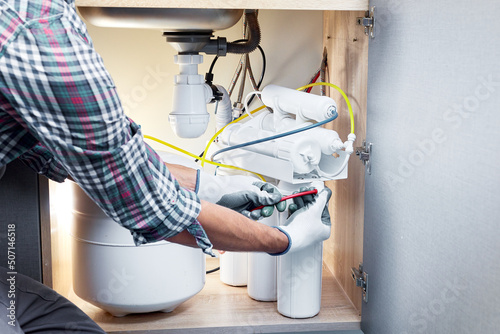 Technician installing or repairing system of water filtration. Plumber hand in gloves replace water filter cartridges at home kitchen.