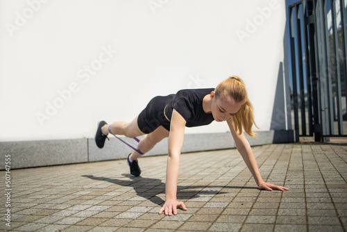 Pretty young fit woman with rubber bands exercise in urban environment.