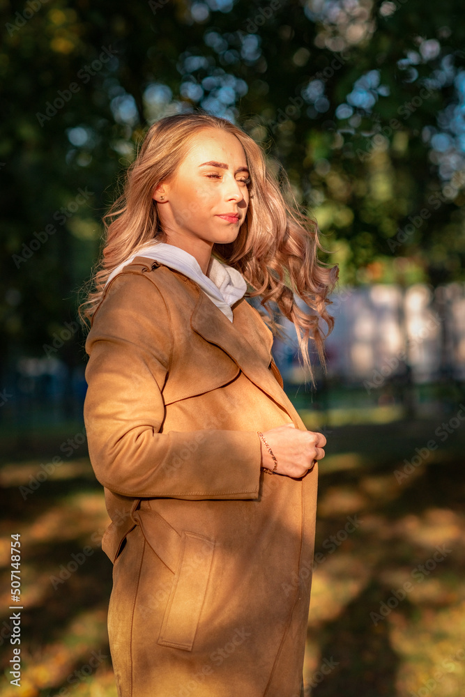 Young beautiful fair-haired girl in a sand-colored raincoat on a walk in the park in early autumn. Young beautiful fair-haired girl in a sand-colored raincoat on a walk in the park in early autumn.