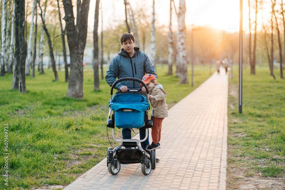 dad with stroller and toddler son walking in the park dad with stroller and toddler son walking in the park