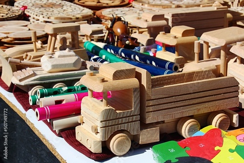 Various wooden toys, trucks, whistles, tanks, buldozer and puzzle displayed in trader booth on outdoor market, sunlit by daylight sunshine. photo