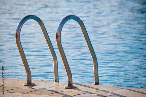 Photo Close up of swimming pool stainless steel handrail descending into tortoise clear pool water