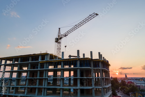 Tower lifting crane and high residential apartment building with monolithic frame under construction at sunset. Real estate development
