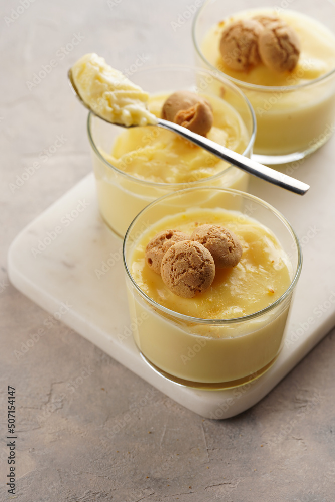 Creamy french vanilla pudding in glass decorated with italian biscuits amaretti on marble board on grey neutral background Creamy french vanilla pudding in glass decorated with italian biscuits amaretti on marble board on grey neutral background