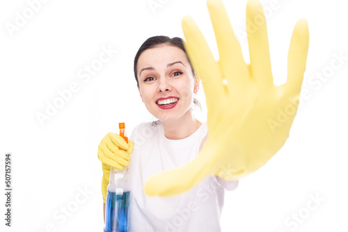 happy female cleaner in yellow gloves for cleaning shows with her hand a stop sign, in her other hand she has window cleaner, white studio background