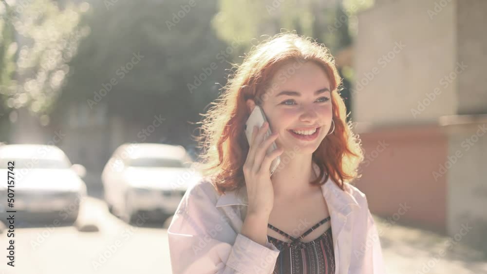 Portrait of attractive red head girl having phone talk. Young beautiful ginger girl at the city street. Happy smiling girl walking forward. Portrait of attractive red head girl having phone talk. Young beautiful ginger girl at the city street. Happy smiling girl walking forward.