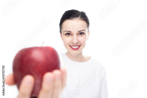 smiling woman in white t-shirt sharing red apple, white studio background