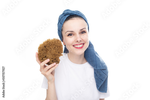 smiling woman in a white t-shirt and a blue towel on her head holds a body washcloth made of natural seaweed in her hand, white studio background