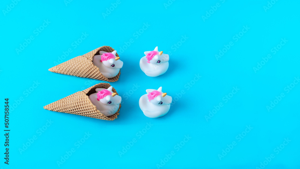 White and pink plastic unicorns coming out of ice cream cones against pastel blue background. Minimal surreal concept for summer holidays banner or card. Flat lay. Copy space.