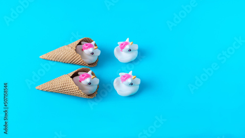 White and pink plastic unicorns coming out of ice cream cones against pastel blue background. Minimal surreal concept for summer holidays banner or card. Flat lay. Copy space.