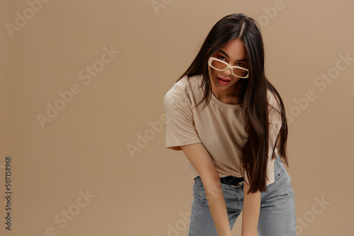 young woman attractive look charmin dark glasses in a t-shirt beige background