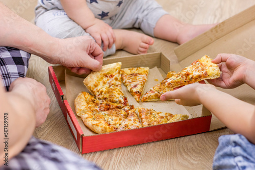 Family hands taking pizza slices on wooden floor background.