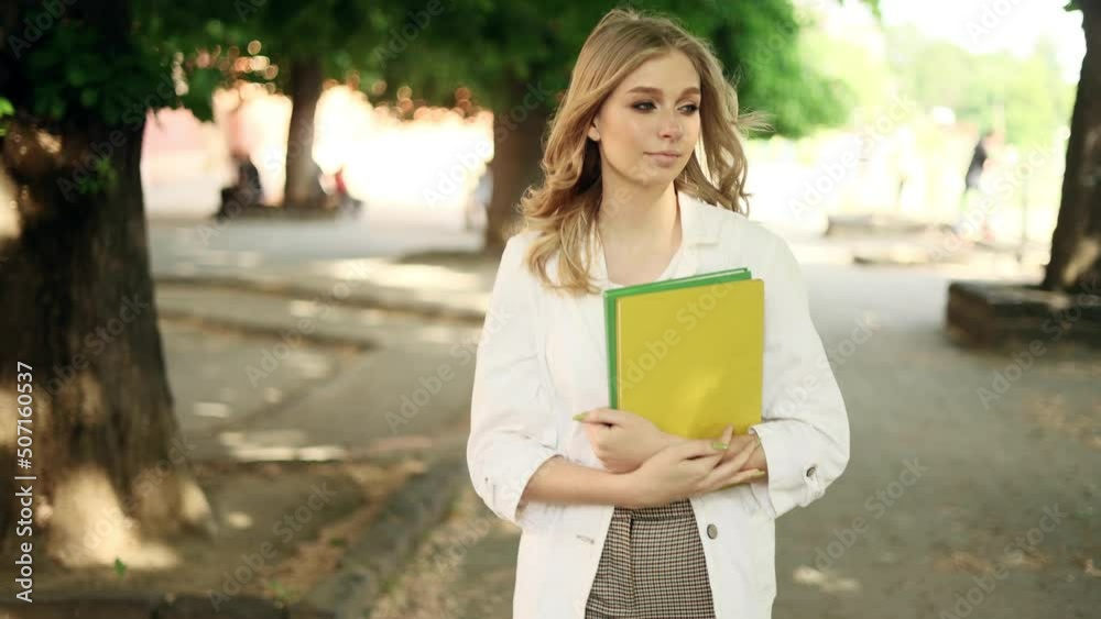 Student girl with eyeglasses walking down with books near the university and looking at the camera. Portrait of attractive blond girl. 