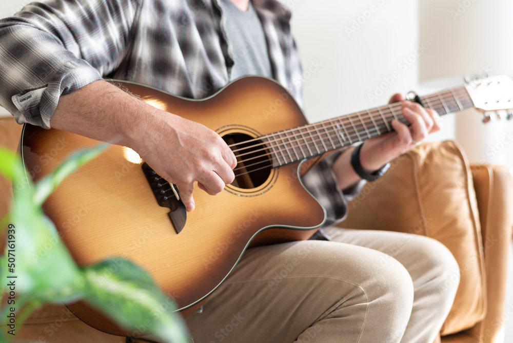 Midsection view of a man sitting on the couch playing guitar