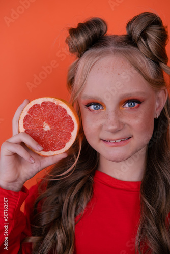 pretty tween girl in orange with a grapefruit isolated on orange background. tropical citrus fruit Grapefruit slices. orange stylish make up. teenager portrait
