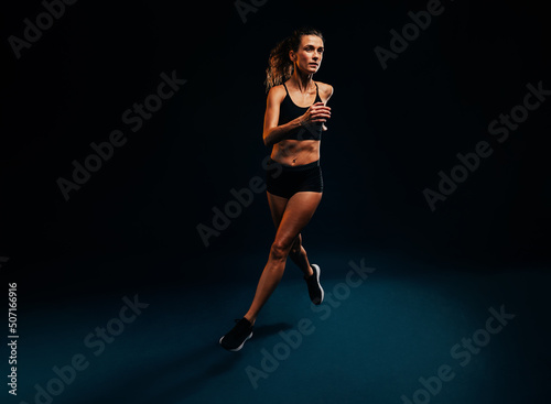 Female runner exercising on black background. Woman jogging and jumping in studio.