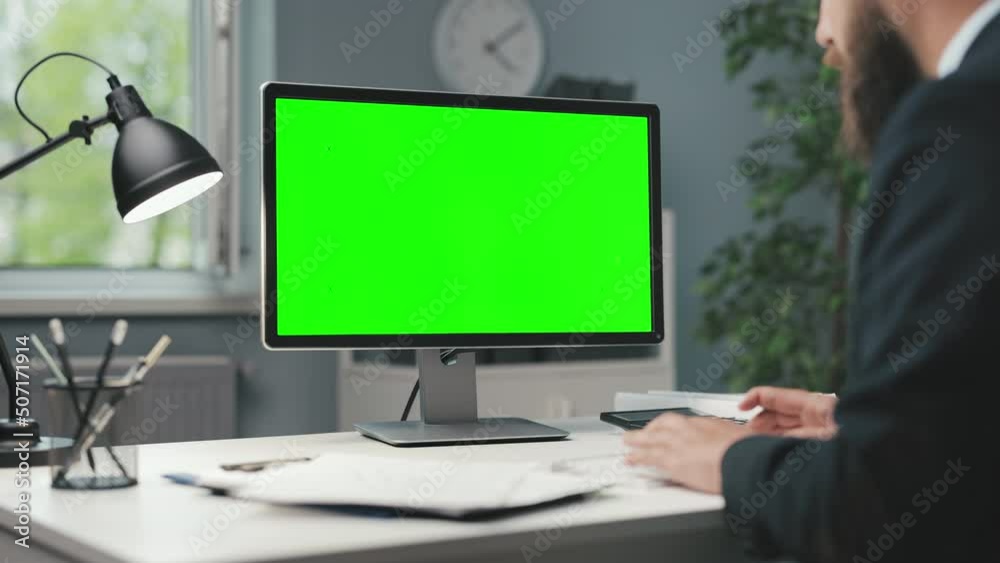 Side view of caucasian bearded man in formal suit sitting at office desk and typing on keyboard. Focus on modern pc with chroma key monitor. Side view of caucasian bearded man in formal suit sitting at office desk and typing on keyboard. Focus on modern pc with chroma key monitor.