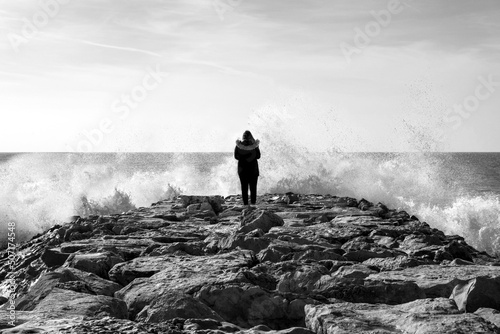 Loney woman on breakwater, splashing waves. photo