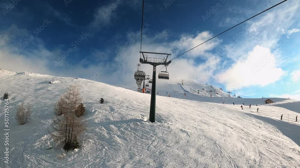 First-person view FPV point of view POV of cable chair ski lift ascend for alpine skiing in Dolomites. Ski resort piste with people skiing in Dolomites in Italy. Ski area Belvedere. Canazei, Italy First-person view FPV point of view POV of cable chair ski lift ascend for alpine skiing in Dolomites. Ski resort piste with people skiing in Dolomites in Italy. Ski area Belvedere. Canazei, Italy