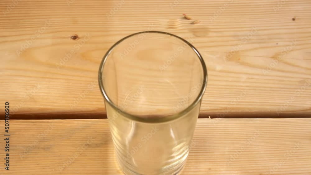 Pouring potable water into glass standing indoor on wooden surface Pouring potable water into glass standing indoor on wooden surface