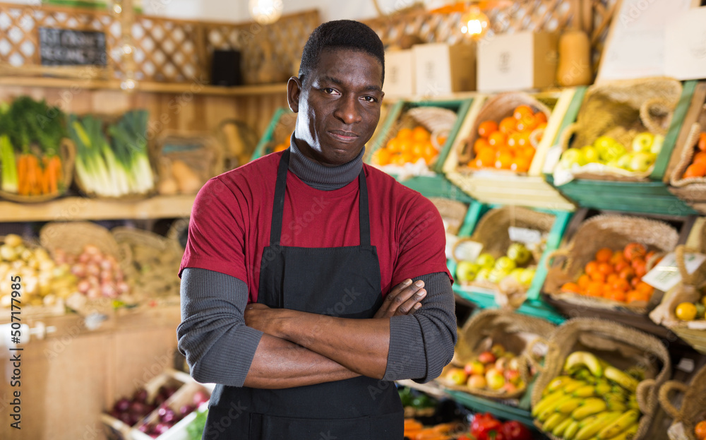 Portrait of confident African American salesman of fruit and vegetable store standing near counter..