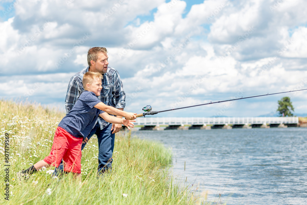 A father and son fishing together on a river bank on a beautiful summer day. A father and son fishing together on a river bank on a beautiful summer day.
