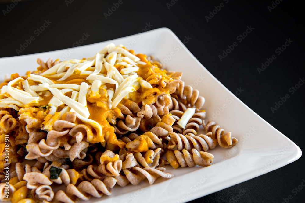 Fusilli pasta with pumpkin sauce and colonial cheese on black background. Fusilli pasta with pumpkin sauce and colonial cheese on black background.
