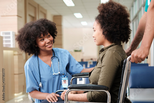 Young African American female doctor with stethoscope in uniform checks injury patient girl in wheelchair at outpatient accident clinic hospital, illness medical clinic examination, healthcare hall.
