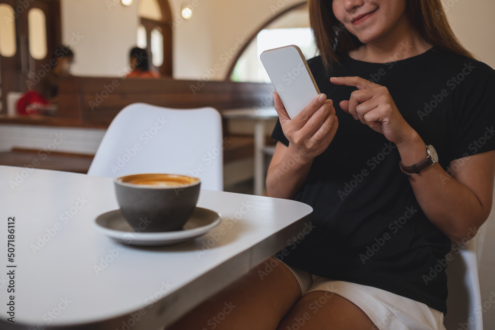 Closeup image of a young woman holding and using mobile phone with coffee cup on the table in cafe Closeup image of a young woman holding and using mobile phone with coffee cup on the table in cafe