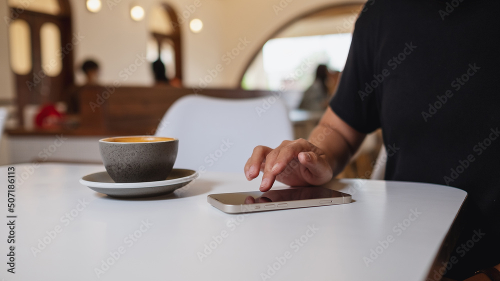 Closeup image of a woman using and touching on mobile phone screen with coffee cup on the table Closeup image of a woman using and touching on mobile phone screen with coffee cup on the table
