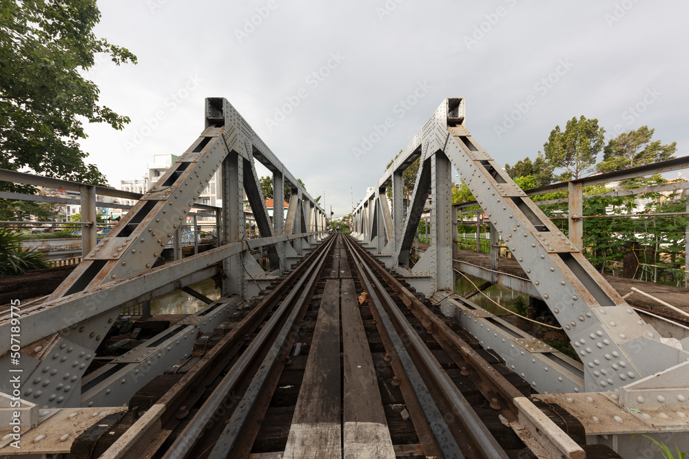 Old French Colonial railway bridge crossing a canal in Saigon or Ho Chi Minh City, Vietnam. Perspective is looking along the tracks